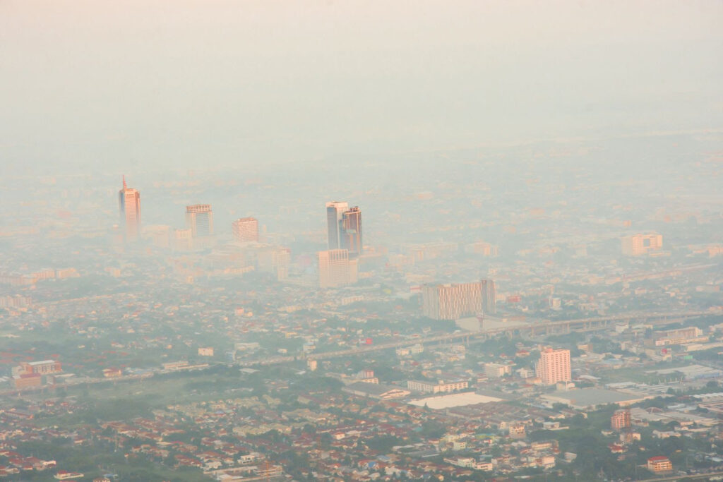 Vista aérea de una ciudad envuelta en una densa capa de smog y contaminación del aire, que dificulta la visibilidad de los edificios y oculta el horizonte. La imagen ilustra los efectos de la contaminación atmosférica en áreas urbanas, destacando la necesidad de adoptar medidas para mejorar la calidad del aire y reducir el impacto ambiental en las ciudades